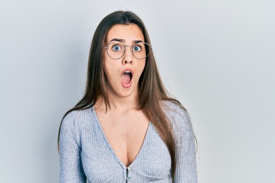 Young brunette teenager wearing casual sweater and glasses afraid and shocked with surprise expression, fear and excited face.