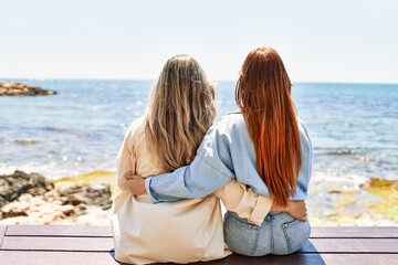 Young lesbian couple of two women in love at the beach. Beautiful women together at the beach in a romantic relationship sitting on a bench