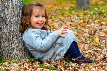 Little girl sitting on the forest floor leaning on a tree