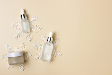 Cosmetic jars on a beige background with snowflakes. Winter care products. Cream, serum, fluid. Minimalism.