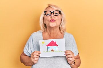 Middle age blonde woman holding house draw looking at the camera blowing a kiss being lovely and sexy. love expression.