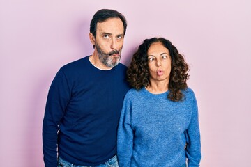 Fototapeta premium Middle age couple of hispanic woman and man hugging and standing together making fish face with lips, crazy and comical gesture. funny expression.