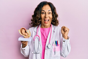 Middle age hispanic doctor woman holding anatomical model of female uterus with fetus screaming...