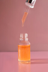A bottle of nail oil with a dropper on a pink background. Front view.