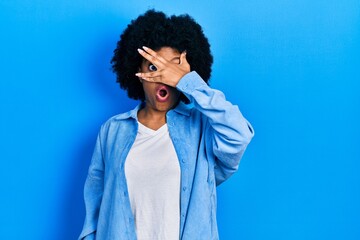 Fototapeta na wymiar Young african american woman wearing casual clothes peeking in shock covering face and eyes with hand, looking through fingers with embarrassed expression.