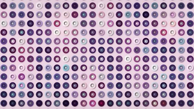Multicolored buttons shimmering isolated on a light pink background, seamless loop. Motion. Silhouettes of tiny rings in purple tones.