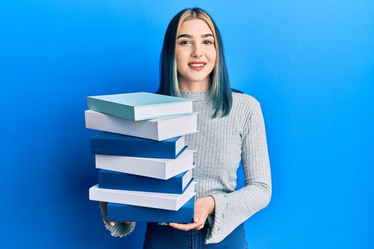Young modern girl holding a pile of books smiling with a happy and cool smile on face. showing teeth.