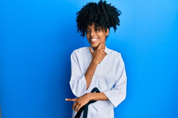 African american woman with afro hair wearing karate kimono and black belt looking confident at the...