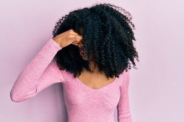 African american woman with afro hair wearing casual pink shirt smelling something stinky and disgusting, intolerable smell, holding breath with fingers on nose. bad smell