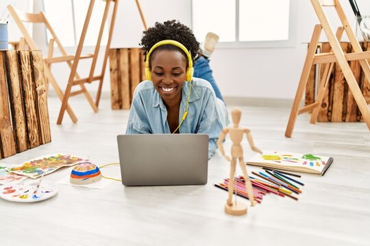Young african american artist woman using laptop and headphones at art studio.