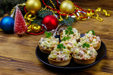 Traditional Russian festive salad Olivier in tartlets and Christmas decorations on wooden table