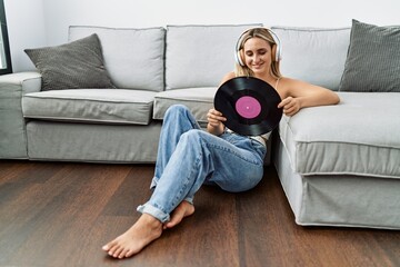 Young blonde woman listening to music holding vinyl disc at home