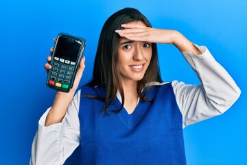 Young hispanic girl holding dataphone stressed and frustrated with hand on head, surprised and...