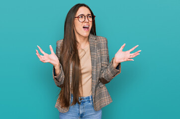 Young hispanic girl wearing business clothes and glasses crazy and mad shouting and yelling with...