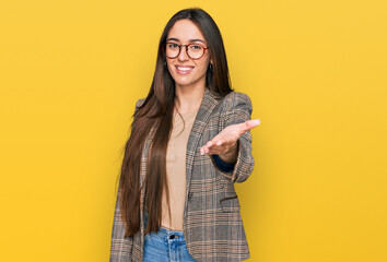 Young hispanic girl wearing business clothes and glasses smiling friendly offering handshake as...