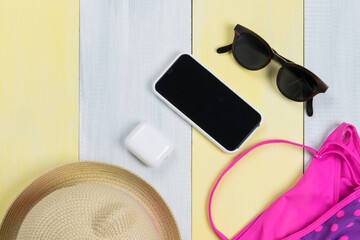 on a gray-yellow surface, a children's swimsuit, sunglasses, a hat and mobile gadgets, a phone and wireless headphones in a case
