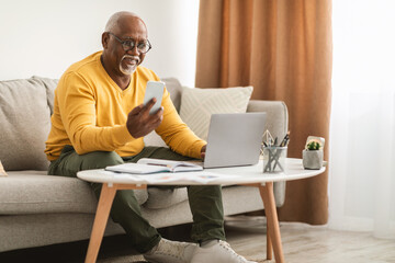 Senior African American Man Using Smartphone And Laptop At Home