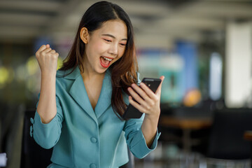 Excited happy woman looking at the phone screen, celebrating an online win, overjoyed young Asian female screaming with joy, isolated over a white blur background