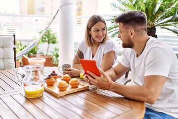 Young couple having breakfast using touchpad at terrace.