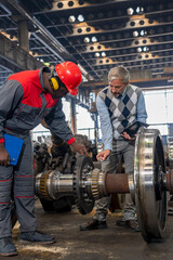 Railway Wheel Set Maintenance At Train Factory - Production Manager Talking To African American Worker In Protective Workwear Next To Train Wheels. Area For Maintenance, Repair And Service Of Trains.