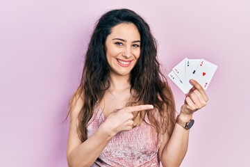 Young hispanic woman holding poker cards smiling happy pointing with hand and finger