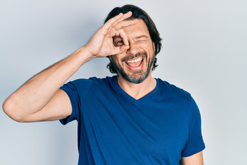 Middle age caucasian man wearing casual clothes smiling happy doing ok sign with hand on eye looking through fingers