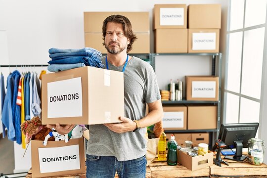 Handsome middle age man holding donations box for charity at volunteer stand skeptic and nervous, frowning upset because of problem. negative person.