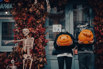 Headless couple holding pumpkin heads by the door on the street