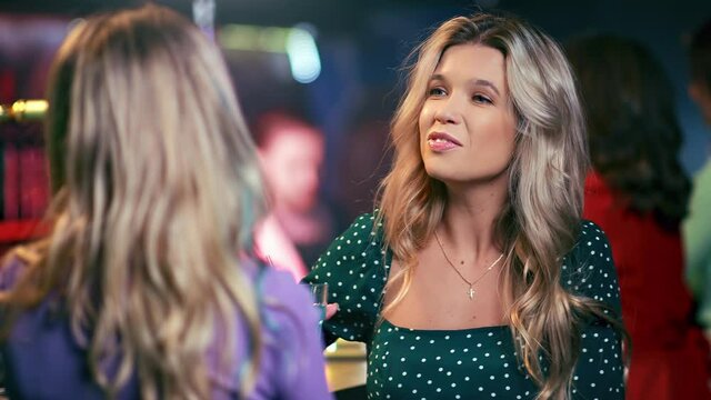 Two beautiful female fashion friends talking smiling relaxing at alcohol bar counter night party 