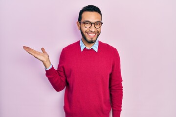 Hispanic man with beard wearing business shirt and glasses smiling cheerful presenting and pointing with palm of hand looking at the camera.