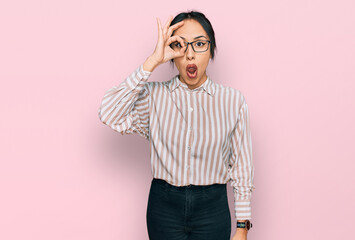 Fototapeta premium Young hispanic girl wearing casual clothes and glasses doing ok gesture shocked with surprised face, eye looking through fingers. unbelieving expression.