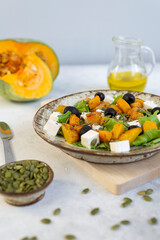 Healthy salad with fried pumpkin, feta cheese, olives, salad greens, pumpkin seeds, olive oil on the dark grey background.
