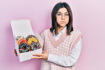 Young brunette woman holding tasty colorful doughnuts puffing cheeks with funny face. mouth...