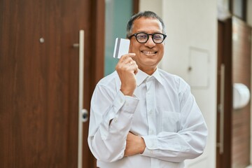 Middle age southeast asian man standing and smiling confident holding credit card by house entrance