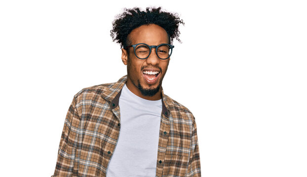 Young african american man with beard wearing casual clothes and glasses winking looking at the camera with sexy expression, cheerful and happy face.
