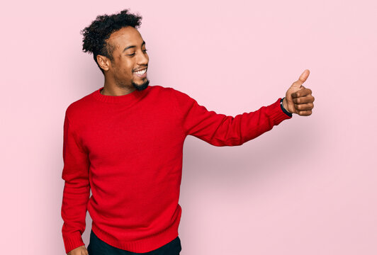Young african american man with beard wearing casual winter sweater looking proud, smiling doing thumbs up gesture to the side