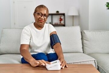 Senior african american woman smiling confident using tensiometer at home