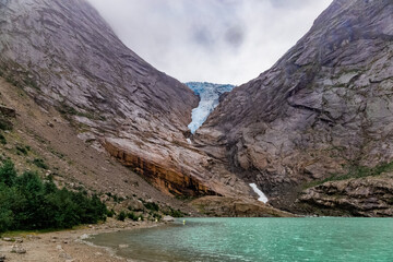 Obraz premium Scenic view on Briksdal glacier, and Norwegian mountains against cloudy dramatic sky