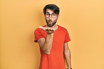 Obraz premium Young hispanic man wearing casual clothes and glasses looking at the camera blowing a kiss with hand on air being lovely and sexy. love expression.