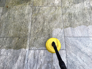 Pressure washer being used to clean grime and dirt from porcelain paving slabs on a garden patio,....