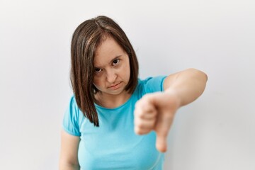 Fototapeta premium Young down syndrome woman standing over isolated background looking unhappy and angry showing rejection and negative with thumbs down gesture. bad expression.
