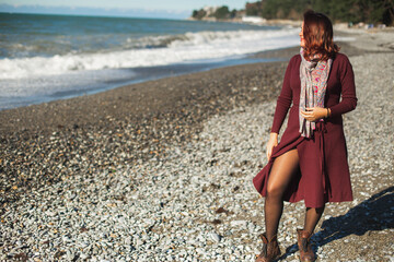 Attractive young woman enjoying on a sea wave on the beach. Cheerful brunette in a burgundy dress...