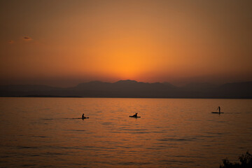 People on a SUP enjoying the beautiful orange sunset at lake Garda in italy 
