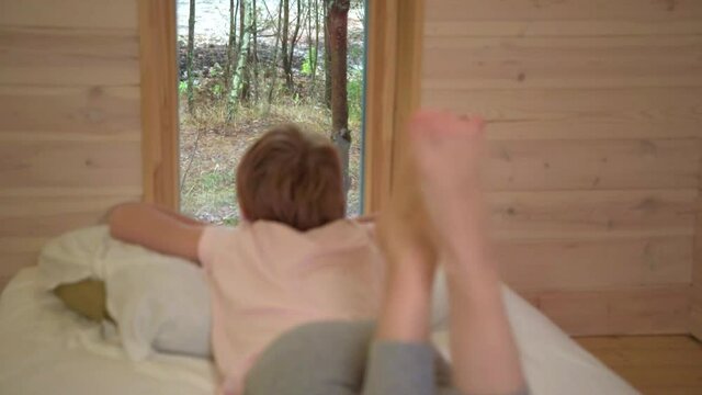 The child lies on the bed and looks out the window. Bare feet close-up. Healthy feet, no signs of flat feet.