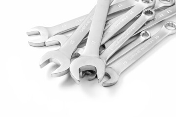A set of steel open-end wrenches of different sizes lying in a chaotic bunch close-up on a white background with a shadow.