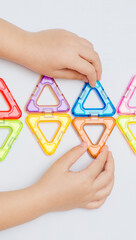 A 5-year-old child collects geometric shapes from multi-colored parts of a magnetic constructor. Flat lay.