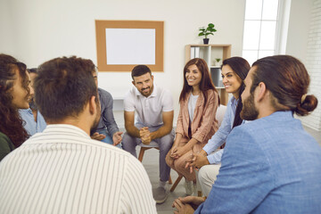 Different people sitting in a circle, talking and smiling during a group therapy session. Team of happy cheerful positive young and mature men and women having a meeting - obrazy, fototapety, plakaty