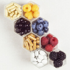 Fresh berries, pills and capsules in honeycomb like hexagonal jars