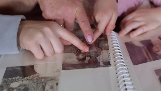 Close-up of hands. Elderly woman grandmother and two granddaughters looking at family photo album showing with hands at different old photos. History and biography concept.