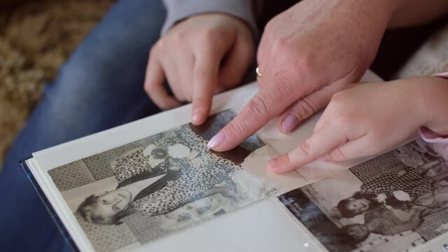 Close-up of hands. Old woman grandmother and two granddaughters looking at family photo album showing with hands at different old photos. Family history and biography concept.